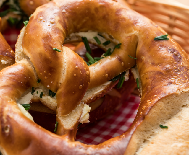 Ein gefüllter Korb mit Brezeln, begleitet von Käse und aromatischen Kräutern